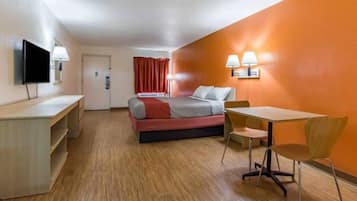 A hotel room with a bed, desk, chair, and TV.