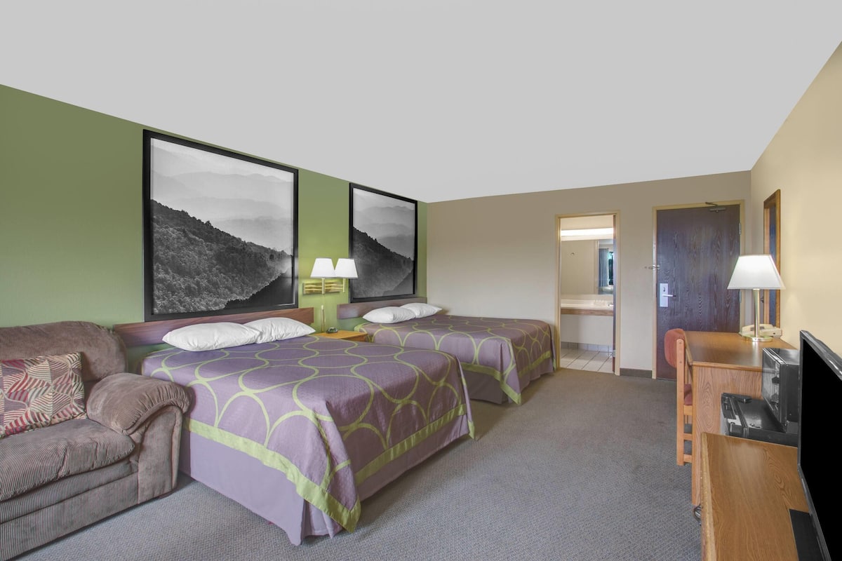 Ein Hotelzimmer mit zwei Betten, einer Schlafcouch, einem Fernseher und einem Schreibtisch.