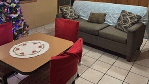 A cozy living room with a dining table, red chairs, a sofa with patterned cushions, a Christmas tree, and a kitchen area with wooden cabinets and a refrigerator. - Super 8 by Wyndham Christiansburg/Blacksburg Area (Christiansburg)