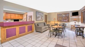 A hotel lobby with a reception desk, a sofa, a dining area with chairs, and a TV mounted on the wall. - Super 8 by Wyndham Christiansburg/Blacksburg Area (Christiansburg)