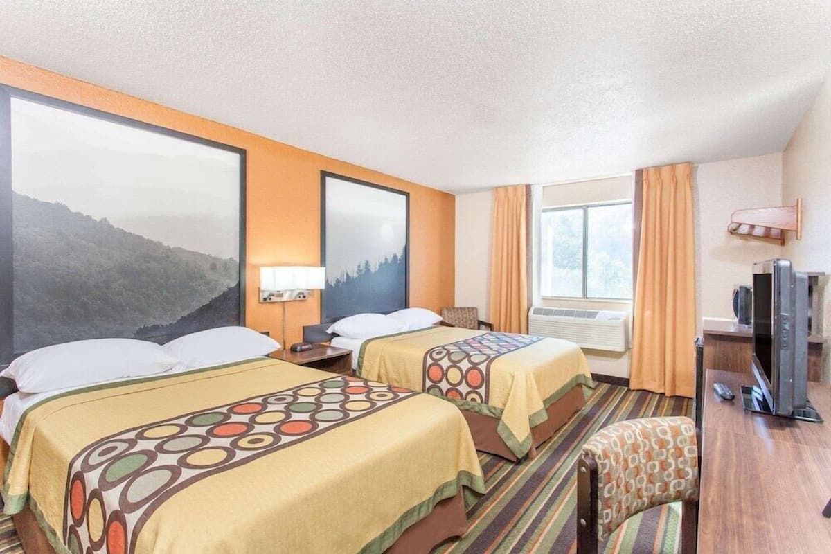 A hotel room with two beds, a television, a desk, and a window with curtains.