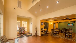 A spacious lobby with a reception desk, a seating area with tables and chairs, and a television mounted on the wall.