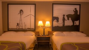 A hotel room with two beds, a nightstand with a lamp, and two framed pictures on the wall.