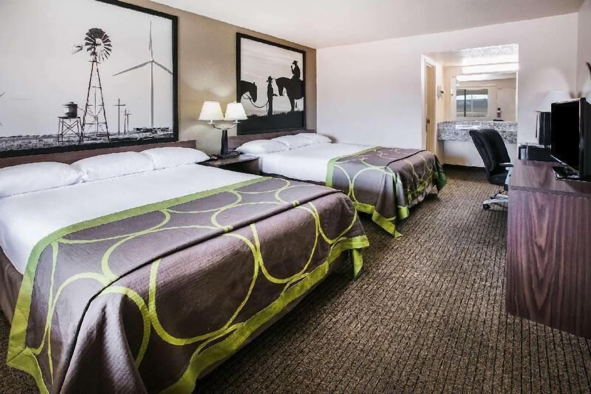 A hotel room with two beds, a desk, a TV, and artwork on the walls.