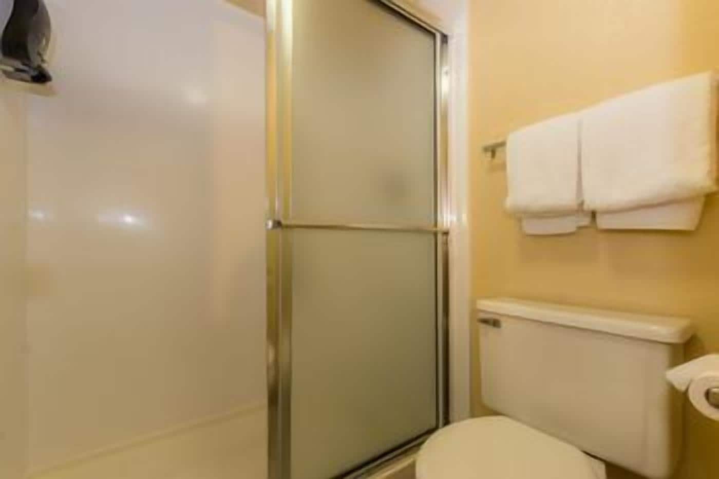 Un baño con cabina de ducha de vidrio, inodoro y perchero con toallas.