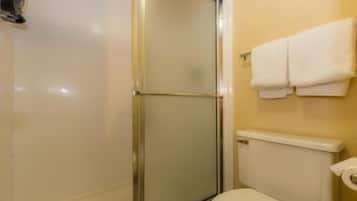 Un baño con cabina de ducha de vidrio, inodoro y perchero con toallas.