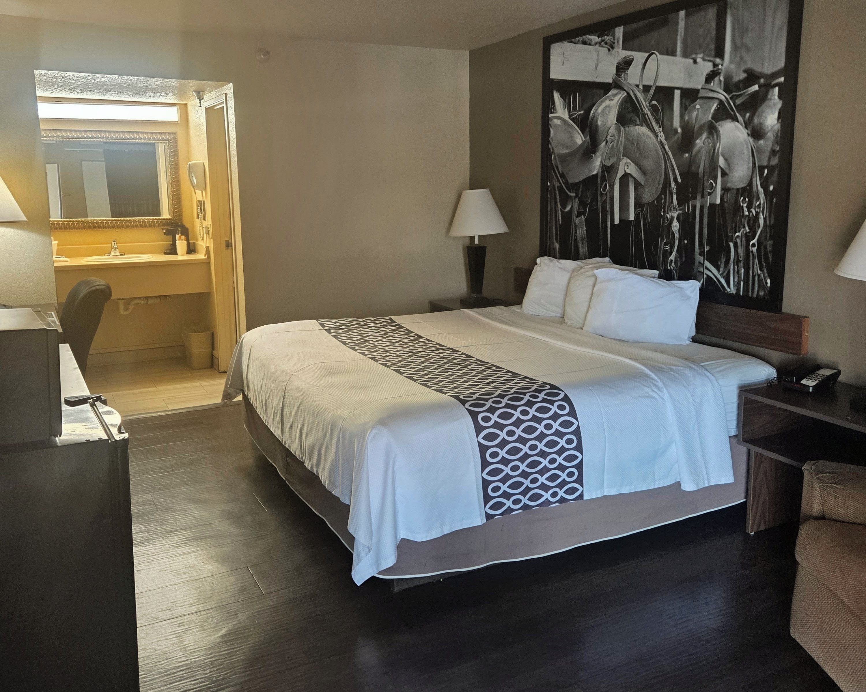 A hotel room with a bed, bedside lamps, a desk, and a large artwork on the wall.