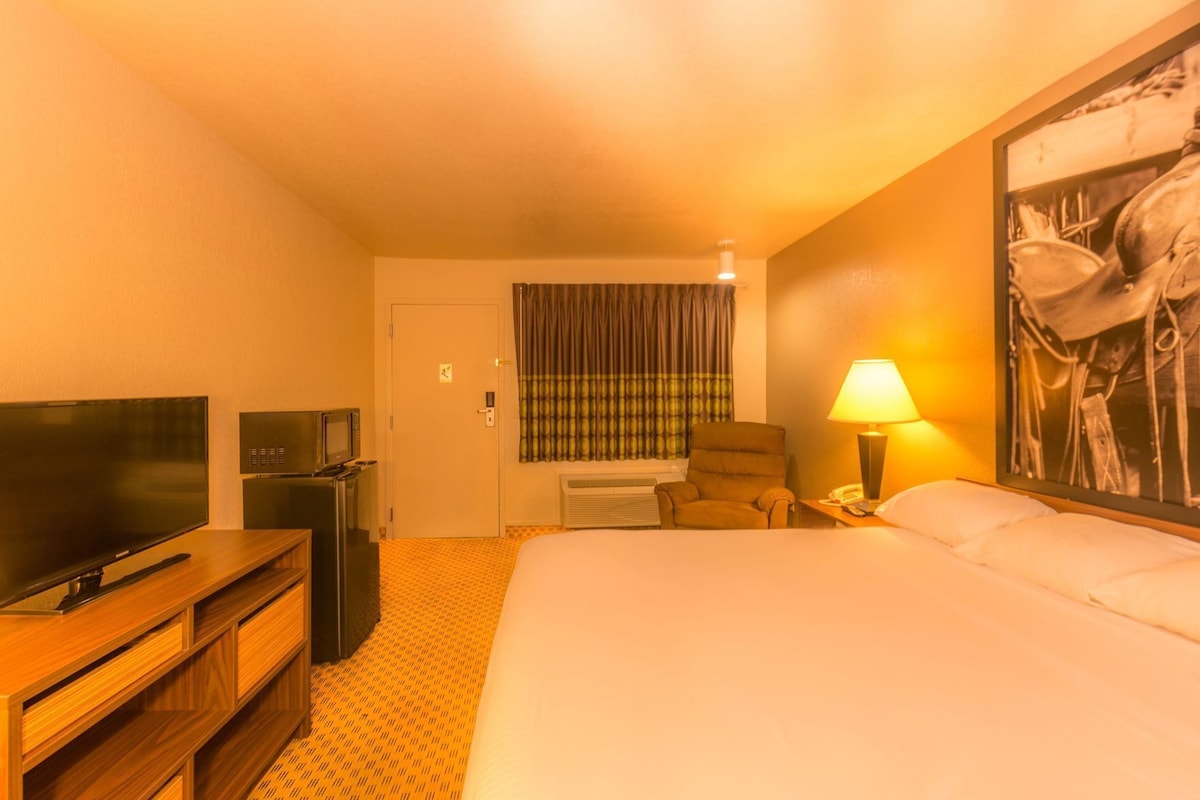 A hotel room with a bed, a television, a chair, a desk with a lamp, and a painting on the wall.