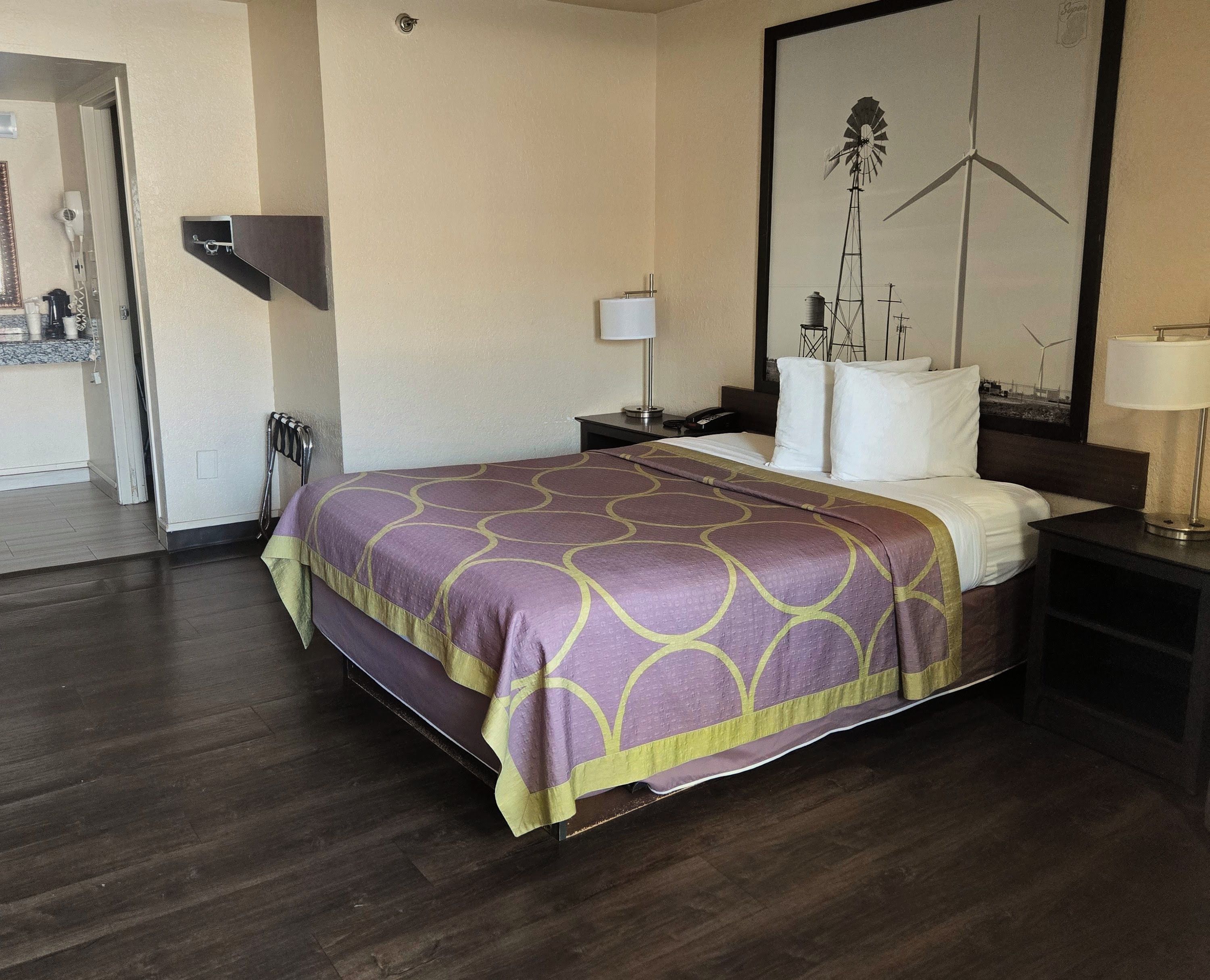 A hotel room with a bed, a nightstand, a lamp, and a painting on the wall.