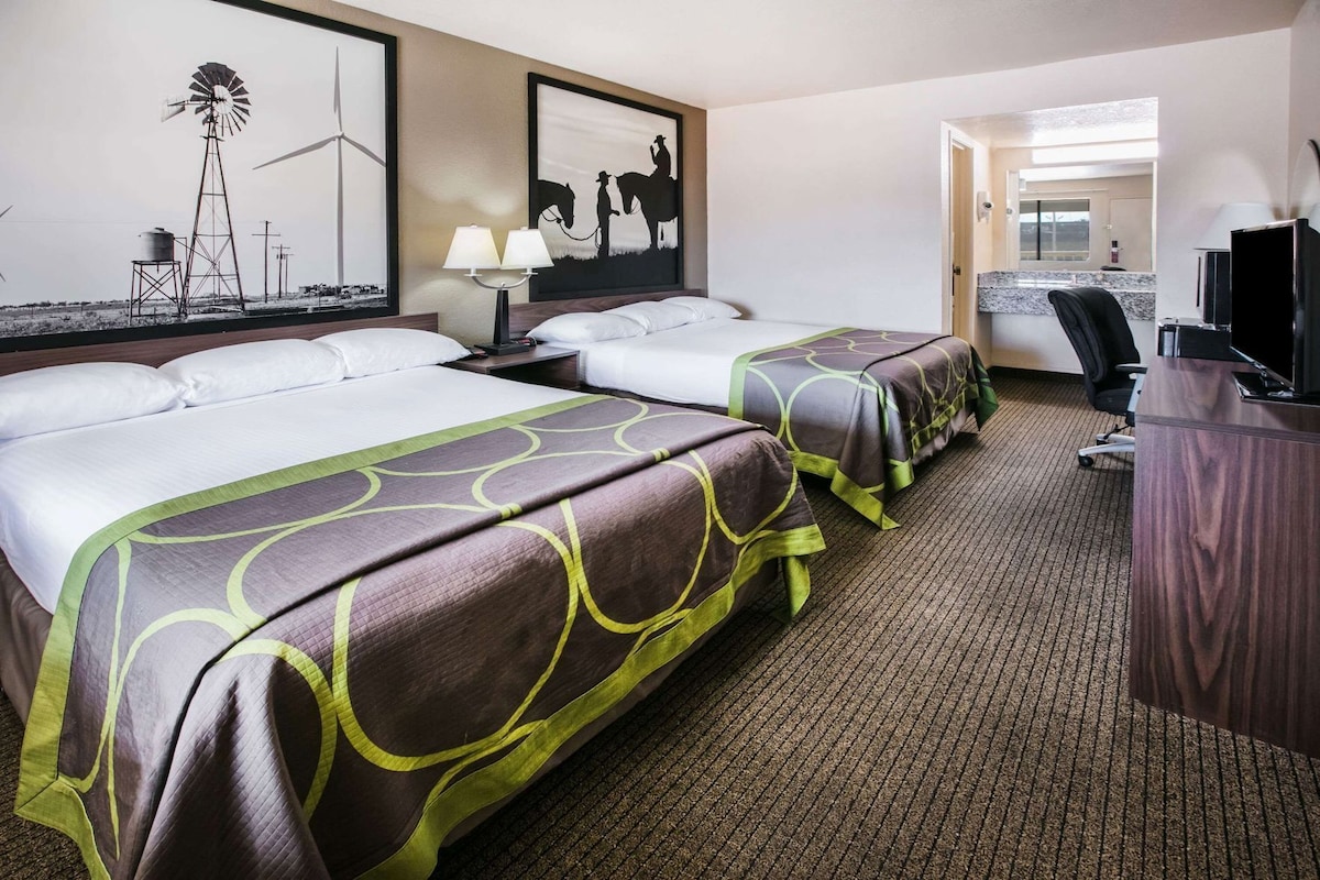 A hotel room with two beds, a desk, a chair, and artwork on the walls.