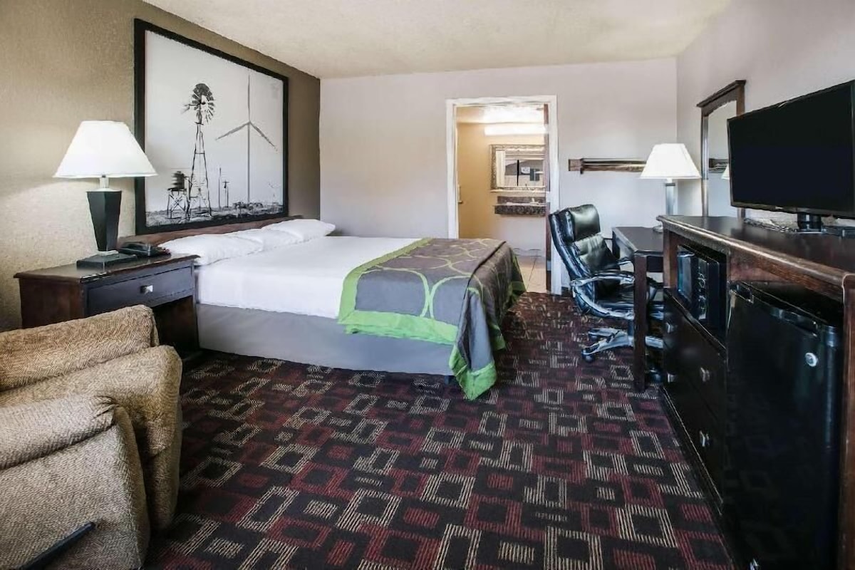 A hotel room with a bed, a desk with a computer, a chair, a television, and a lamp.
