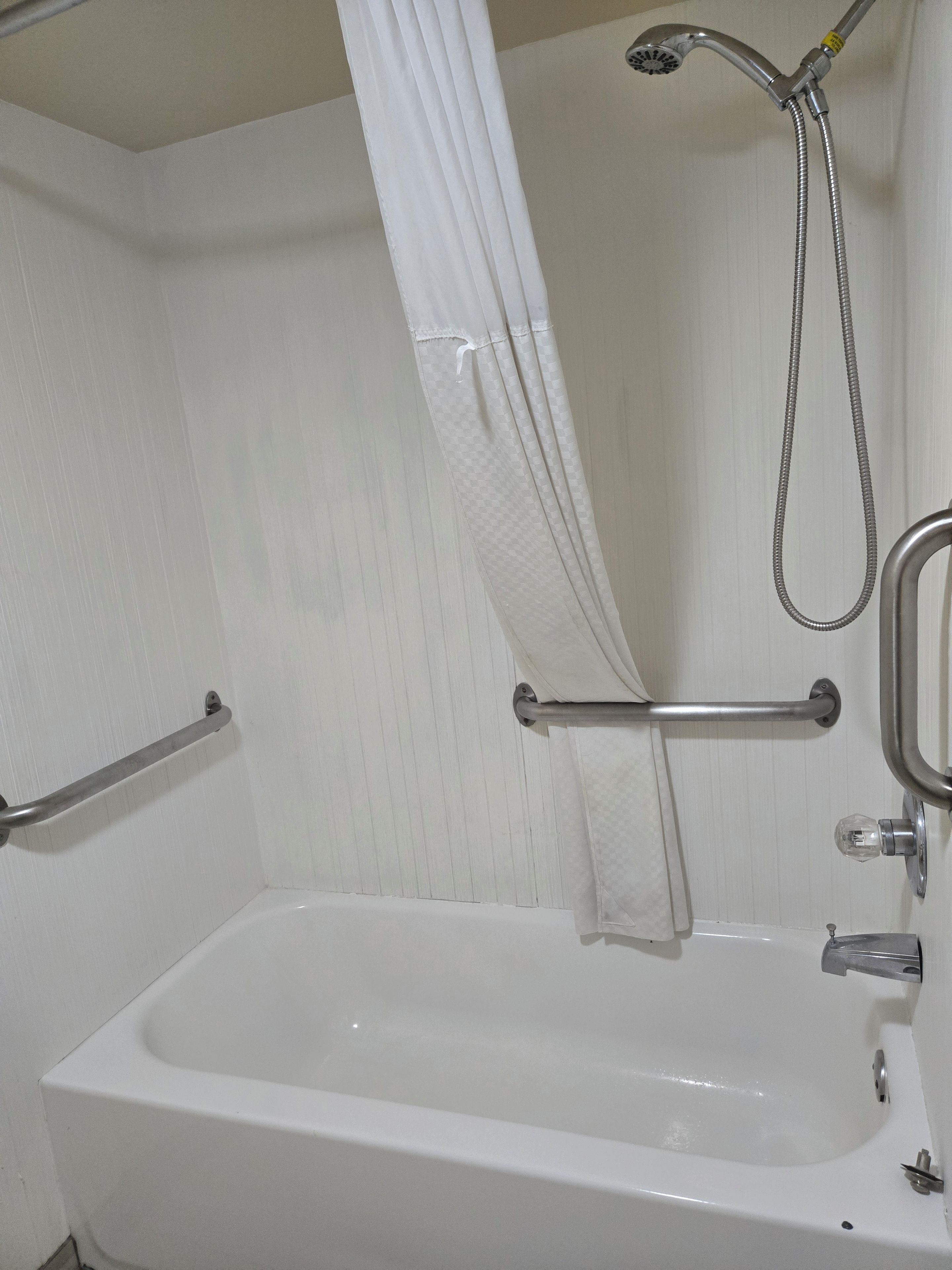 A bathroom with a white bathtub, a shower with a handheld showerhead, and a grab bar.