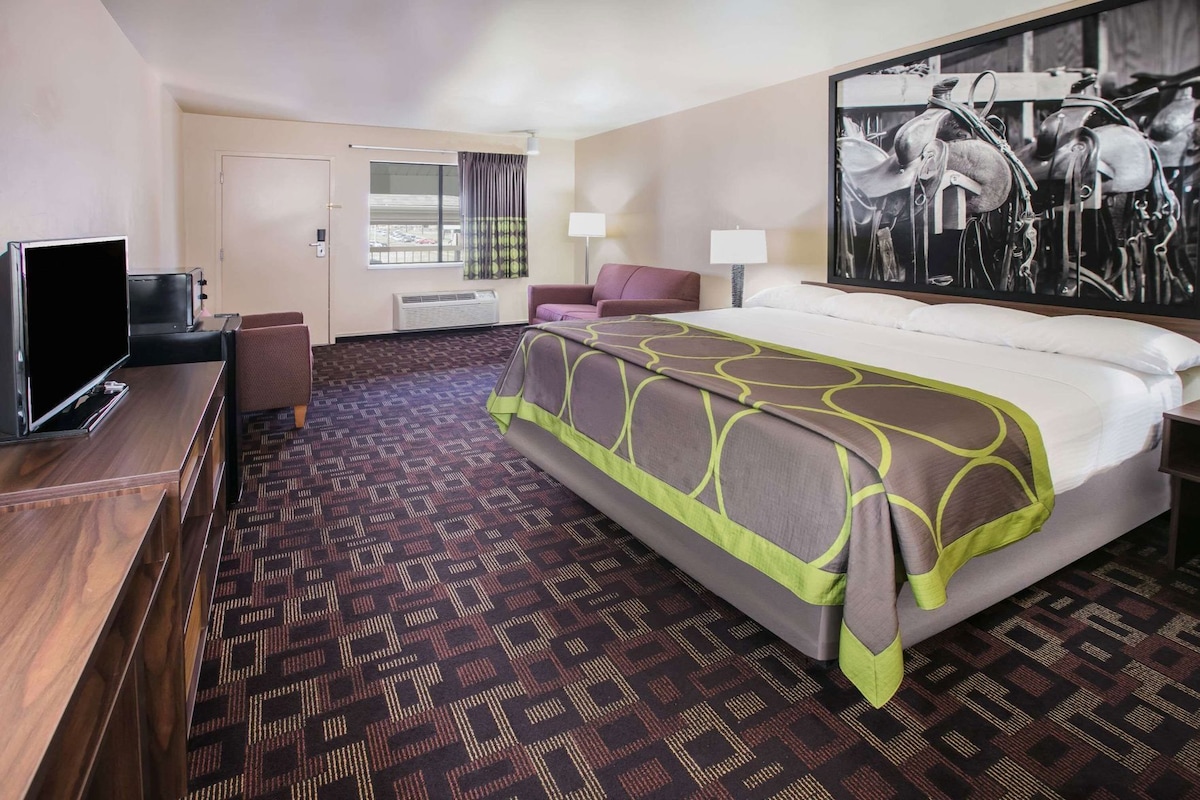 A hotel room with a bed, a TV, a desk, a chair, a lamp, and a painting on the wall.