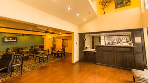 A hotel lobby with a reception desk, dining area with tables and chairs, and a ceiling fan.