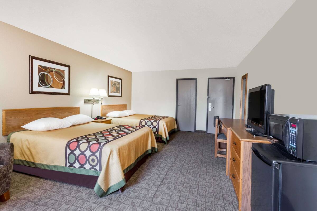 Habitación de hotel con dos camas, un escritorio, un televisor, una lámpara y dos puertas.