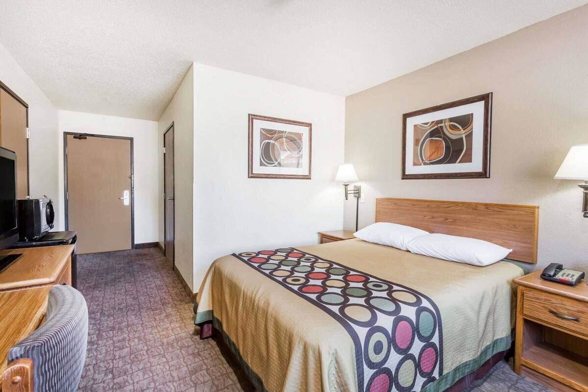 Habitación de hotel con cama, escritorio con televisor, lámpara y dos cuadros en la pared.