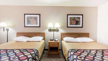 Una habitación de hotel con dos camas, cada una con cabecero de madera, una mesita de noche con lámpara y cuadros en la pared.
