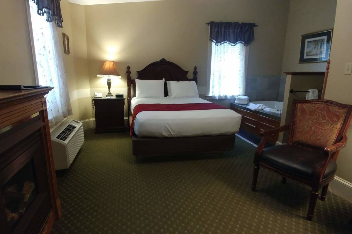Ein Hotelzimmer mit einem großen Bett, einem Sessel, einem Schreibtisch, einer Lampe und einem Kamin.