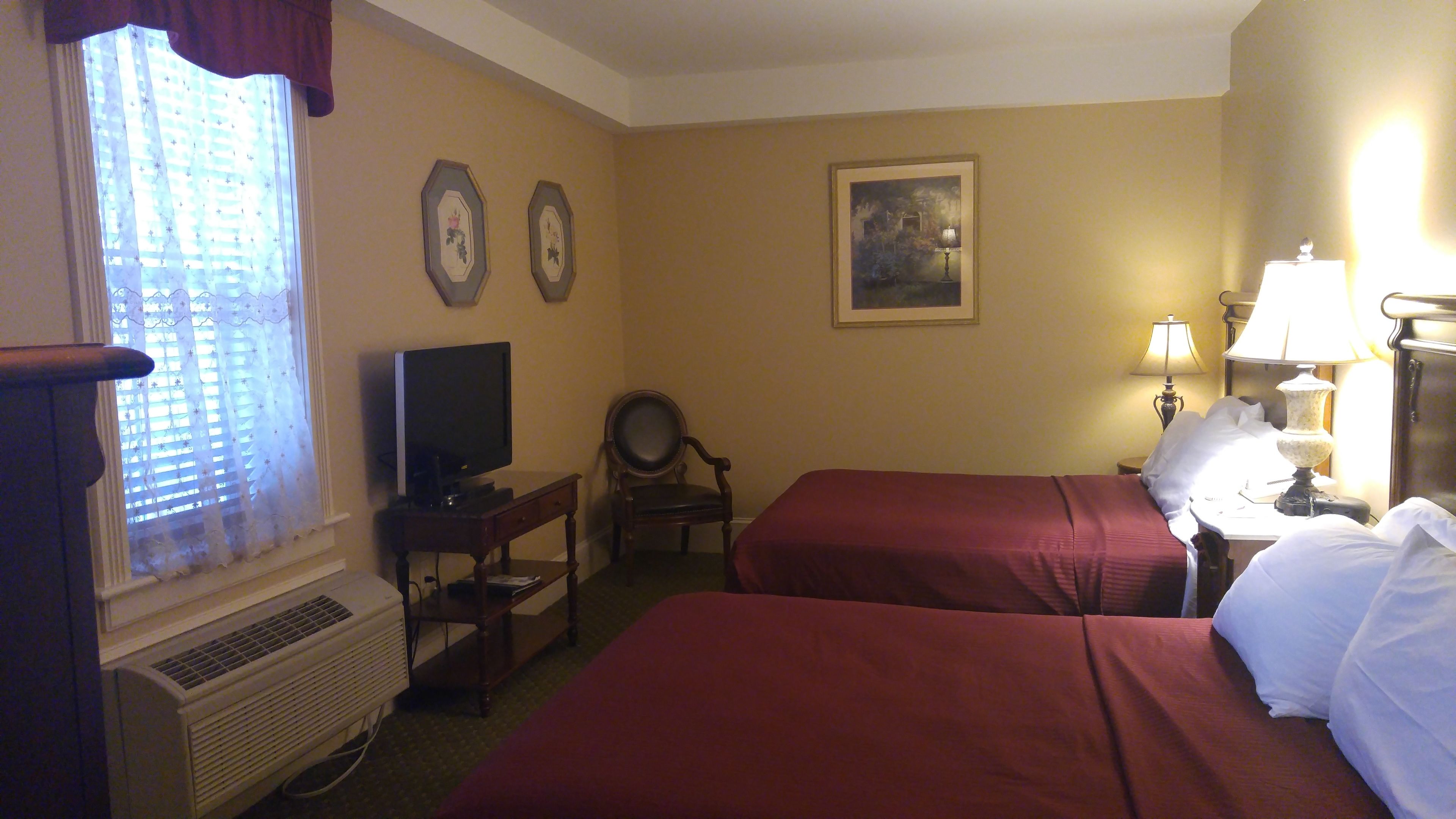 A hotel room with two beds, a television, a chair, a desk, and a painting on the wall.