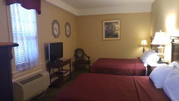 Una habitación de hotel con dos camas, televisión, una silla, escritorio y un cuadro en la pared.