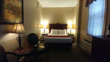 Een hotelkamer met een bed, twee bedlampen, een stoel, een bureau, een schilderij en een raam met jaloezieën.
