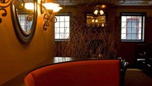 A restaurant interior with a curved red bench, wall-mounted lamps, and a ceiling with exposed beams. - Inn at Jim Thorpe (Jim Thorpe)