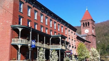 A historic building with a clock tower, featuring a central courtyard with a balcony, surrounded by parked cars.