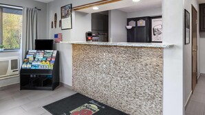 Un espace d’accueil avec un comptoir en pierre, un paillasson, un présentoir à magazines et une horloge murale.