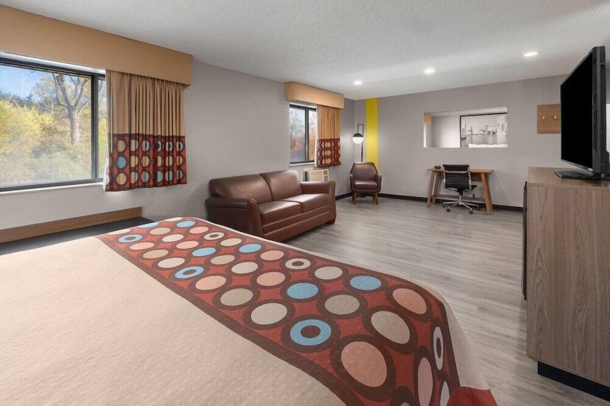 A hotel room with a large bed, a sofa, a desk, a chair, a television, and a window with curtains.
