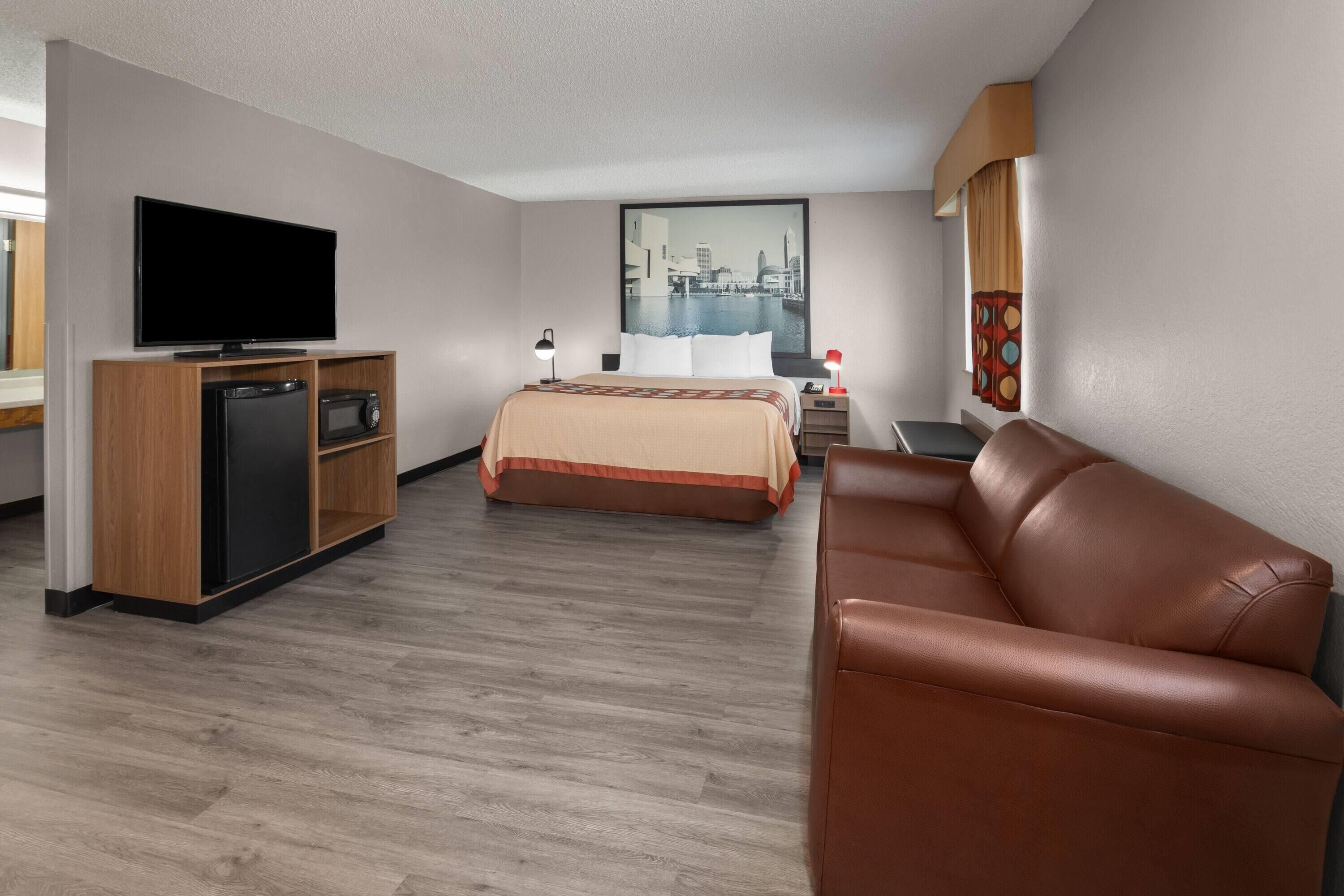 A hotel room with a bed, a TV, a desk with a computer, a leather sofa, and a cityscape view.