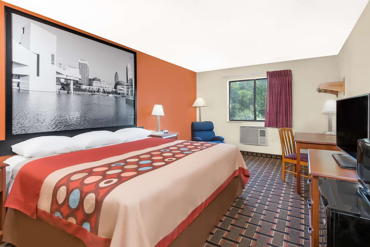 A hotel room with a bed, a desk, a chair, a television, and a large window.