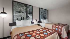 Une chambre d’hôtel avec deux lits, chacun recouvert d’une couvre-lit à motifs, une grande fenêtre donnant sur une maison et des arbres, et une lampe sur pied.
