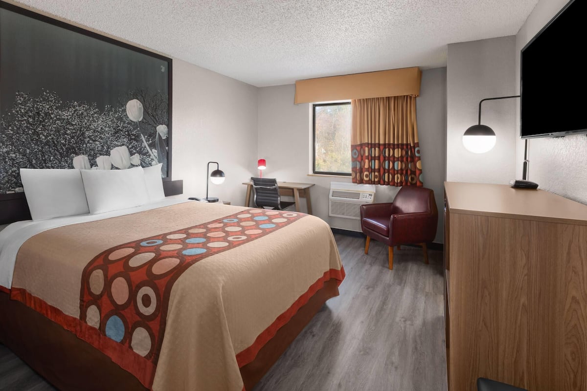 A hotel room with a large bed, a desk, a chair, a TV, and a window with curtains.
