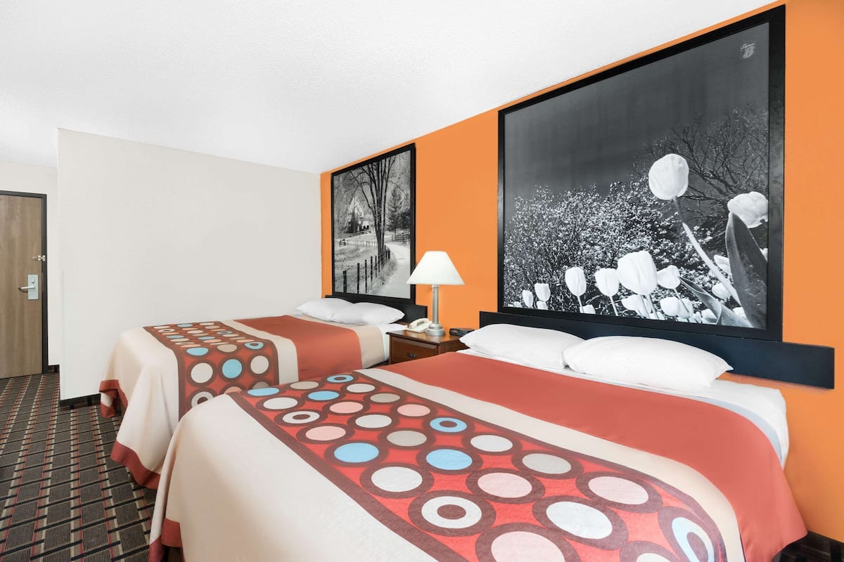 A hotel room with two beds, a nightstand, a lamp, and two large framed pictures on the wall.