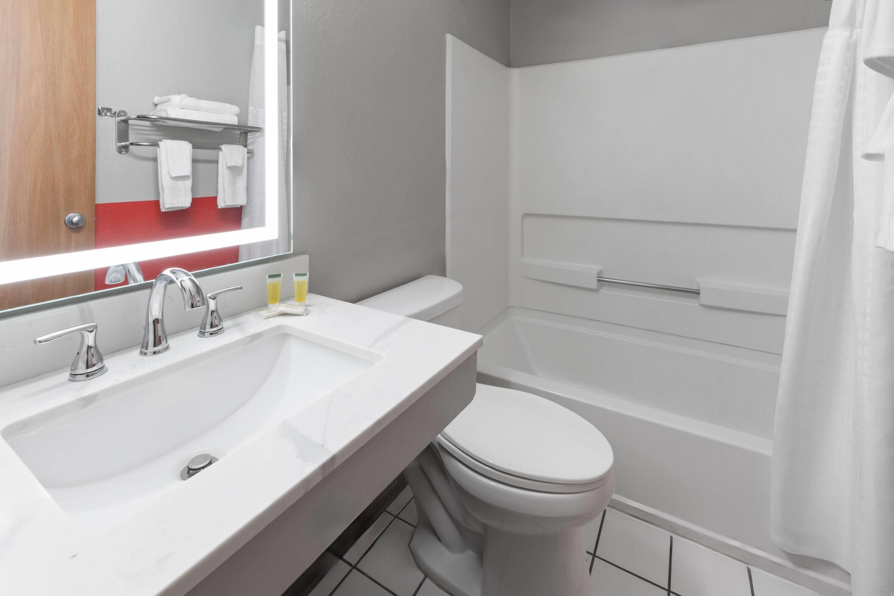 A modern bathroom with a white sink, two faucets, a toilet, and a bathtub.