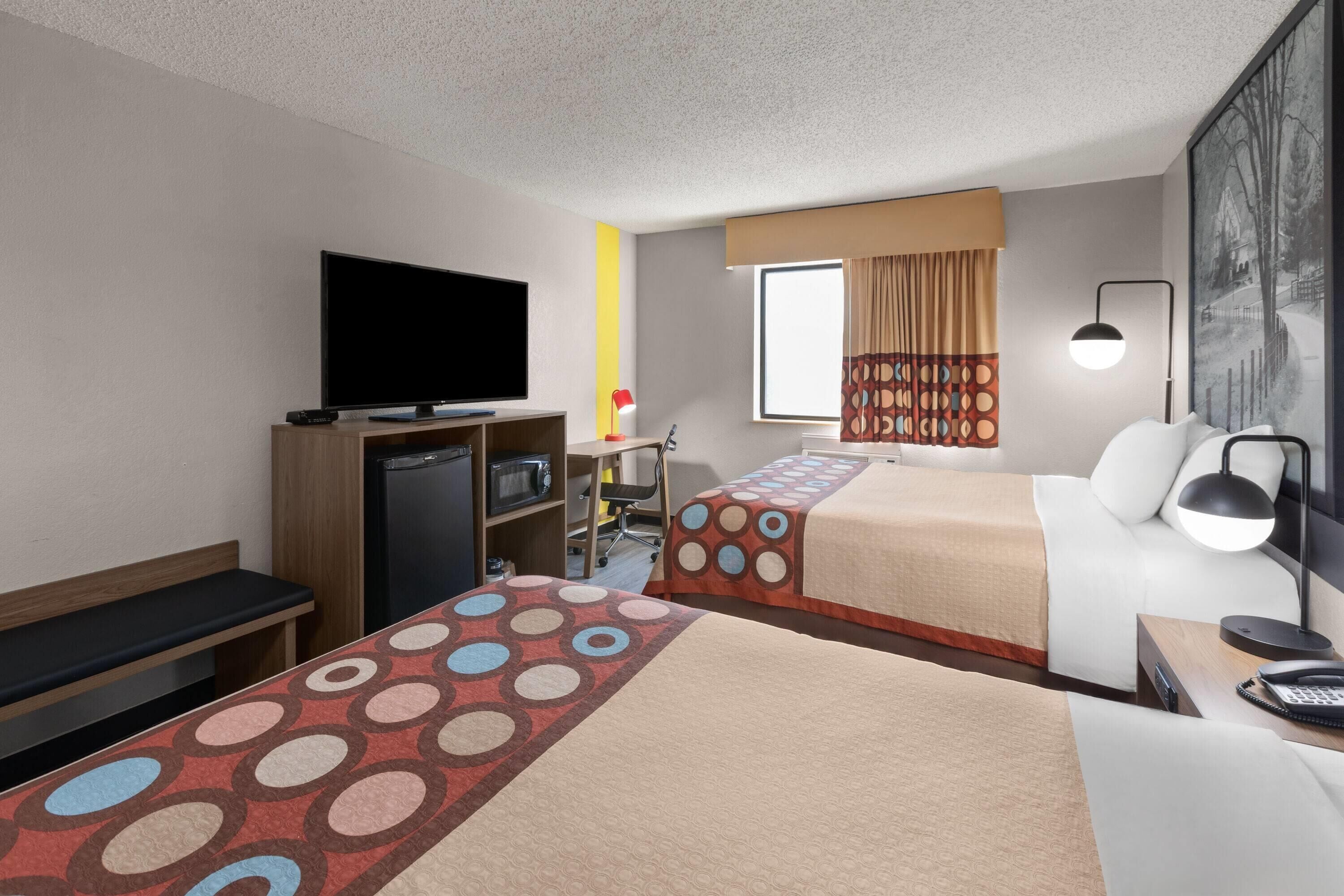 A hotel room with two beds, a TV, a desk, a chair, a desk lamp, and a window with curtains.