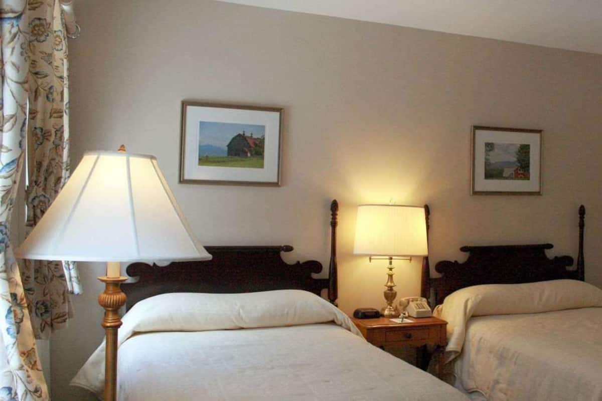A hotel room with two single beds, a nightstand with a lamp, and two framed pictures on the wall.