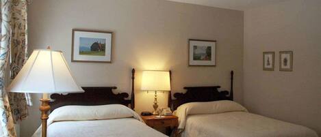 A hotel room with two single beds, a nightstand with a lamp, and two framed pictures on the wall.