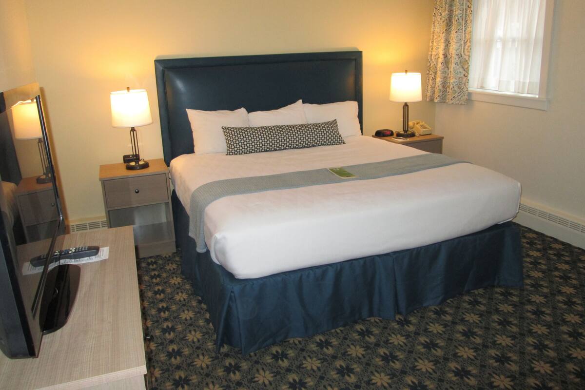 A hotel room with a large bed, two bedside tables, a desk with a chair, a lamp, and a telephone.