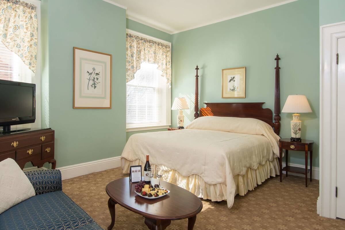 A bedroom with a bed, a bedside table with a lamp, a dresser, a television, and a framed picture on the wall.