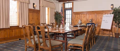 A conference room with a long table, wooden chairs, and a whiteboard.