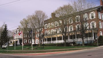A multi-story brick building with a central porch, flagpoles, and a street view.
