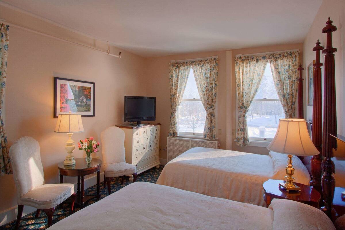 A hotel room with two beds, a television, a desk with a lamp, a chair, and a dresser.