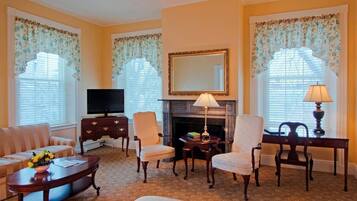 A living room with a sofa, armchairs, a fireplace, a television, and a table with lamps.