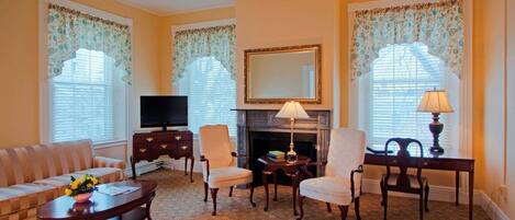 A living room with a sofa, armchairs, a fireplace, a television, and a table with lamps.