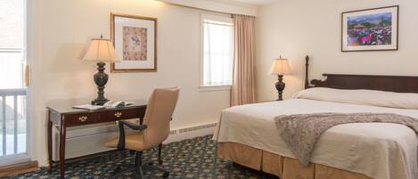 A hotel room with a bed, desk, chair, two lamps, a framed picture, and a window with curtains.