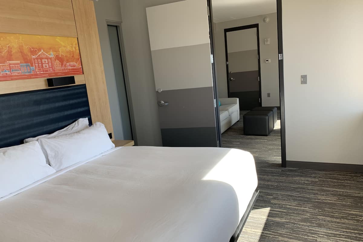 A hotel room with a large bed, a sofa, a small table, and a painting on the wall.