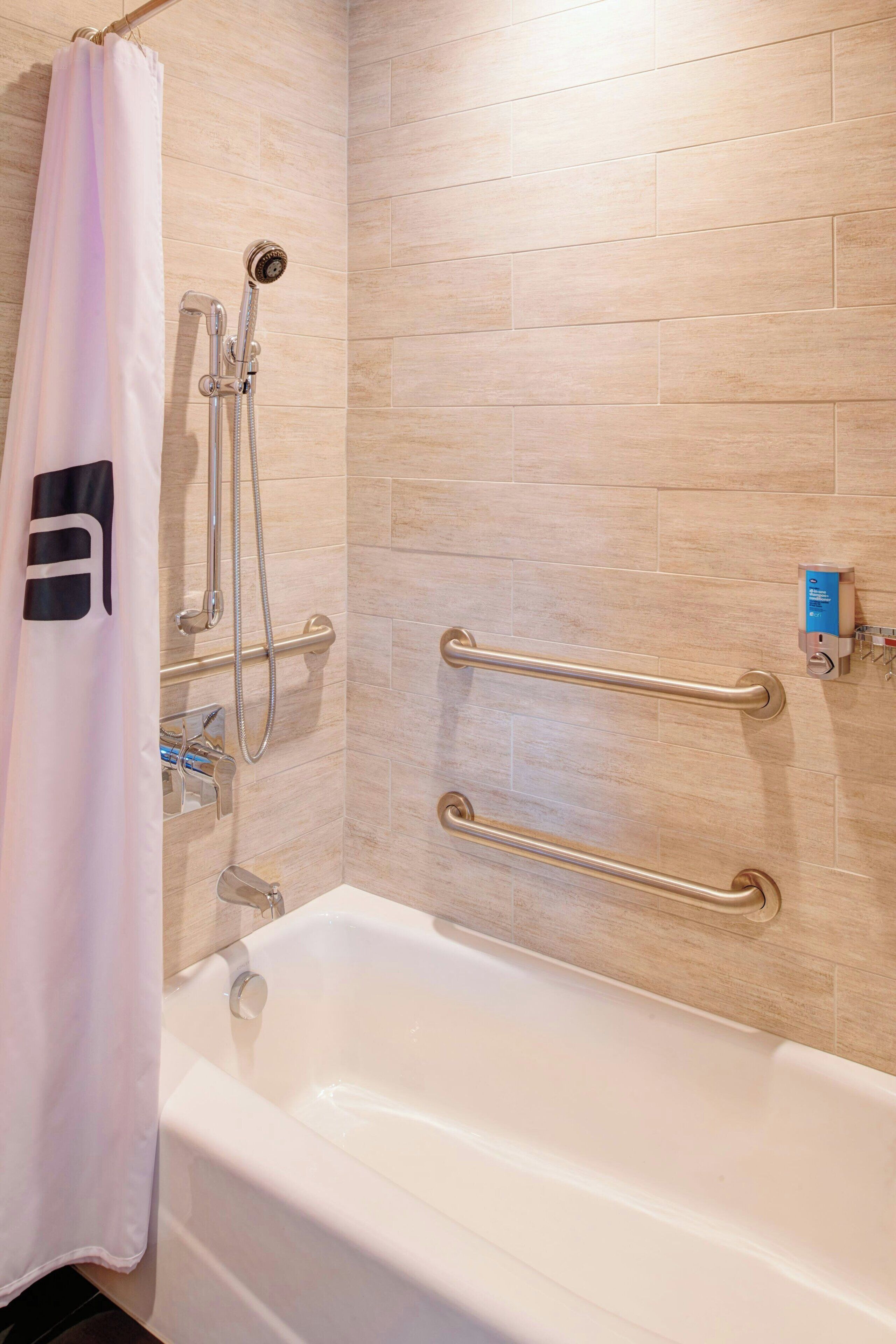 Un baño con bañera, ducha con cabezal de ducha manual y barandilla.