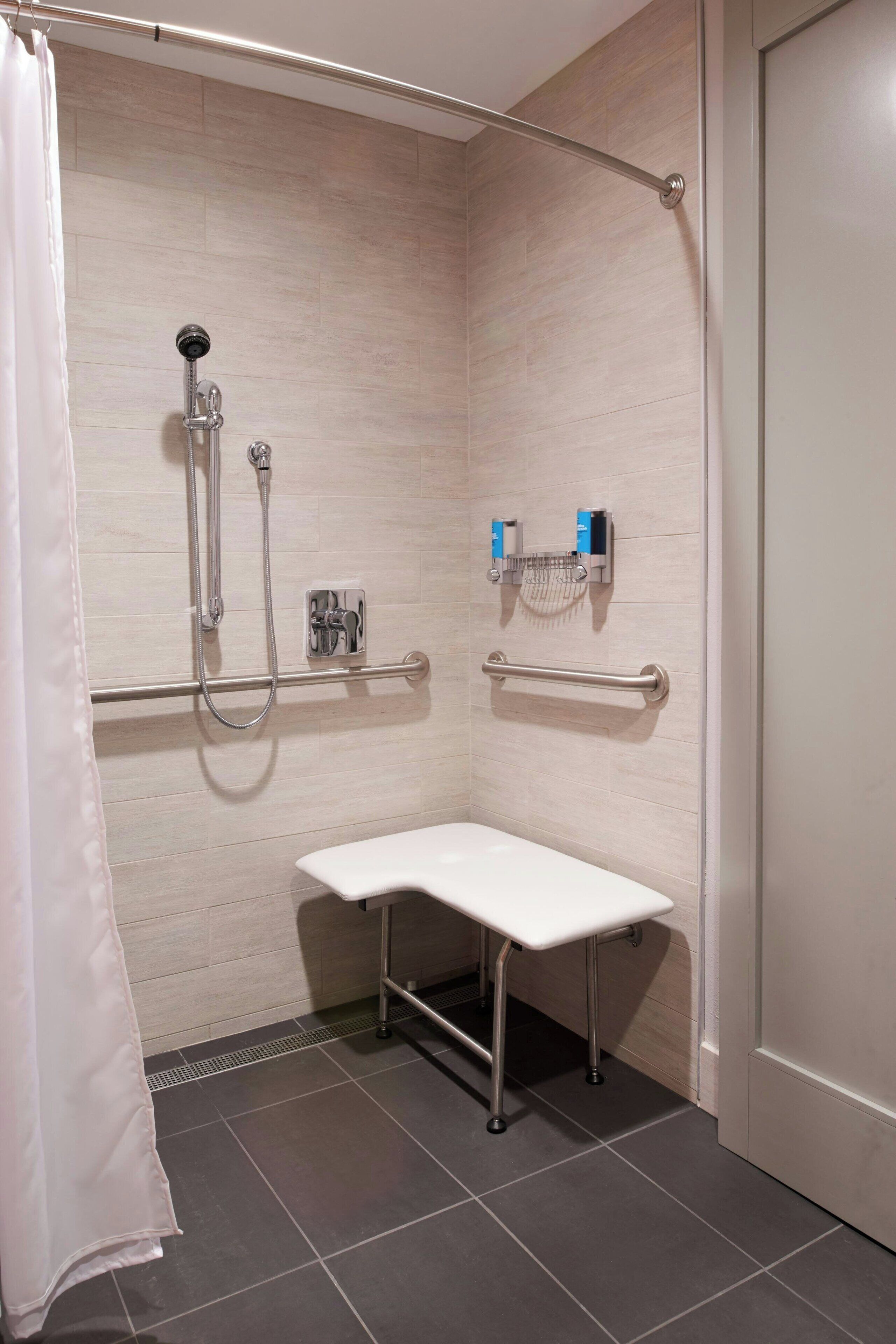 A small, modern bathroom with a shower, grab bars, a toilet, and a towel rack.