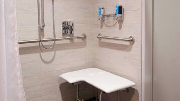A small, modern bathroom with a shower, grab bars, a toilet, and a towel rack.